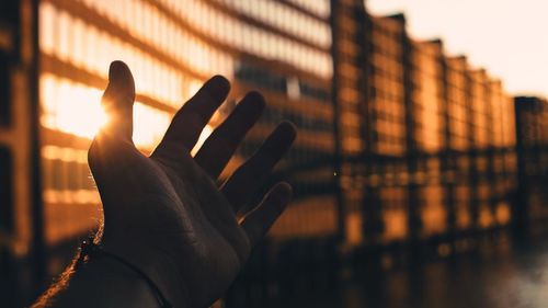 Close-up of human hand against sunset sky