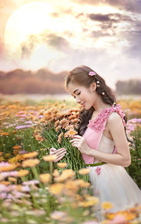 Young woman with pink flowers against sky during sunset