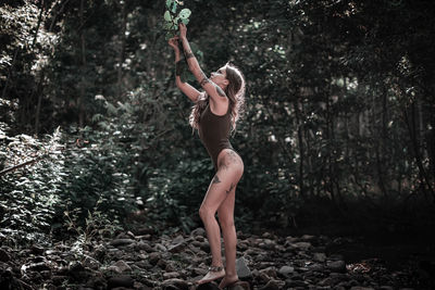 Full length of woman standing by tree in forest