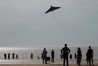 Rear view of people at beach against sky