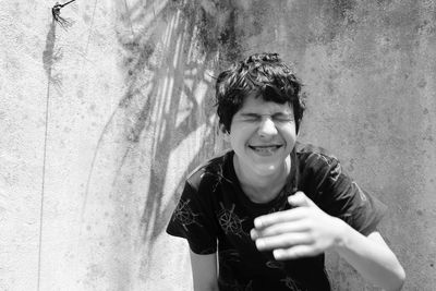 Playful young man with eyes closed standing against wall