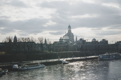 View of buildings by river against cloudy sky