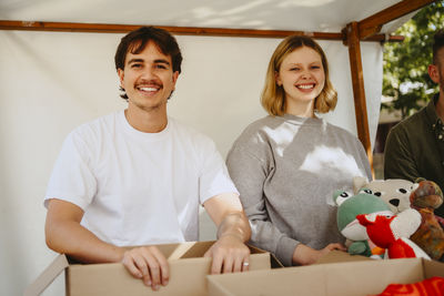 Portrait of happy volunteers with stuffed toys below tent at community center