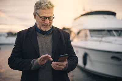 Senior man using smart phone while standing at harbor