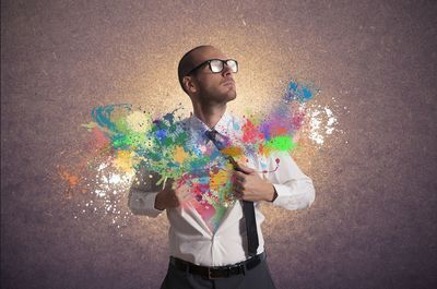 Man holding umbrella standing against multi colored wall