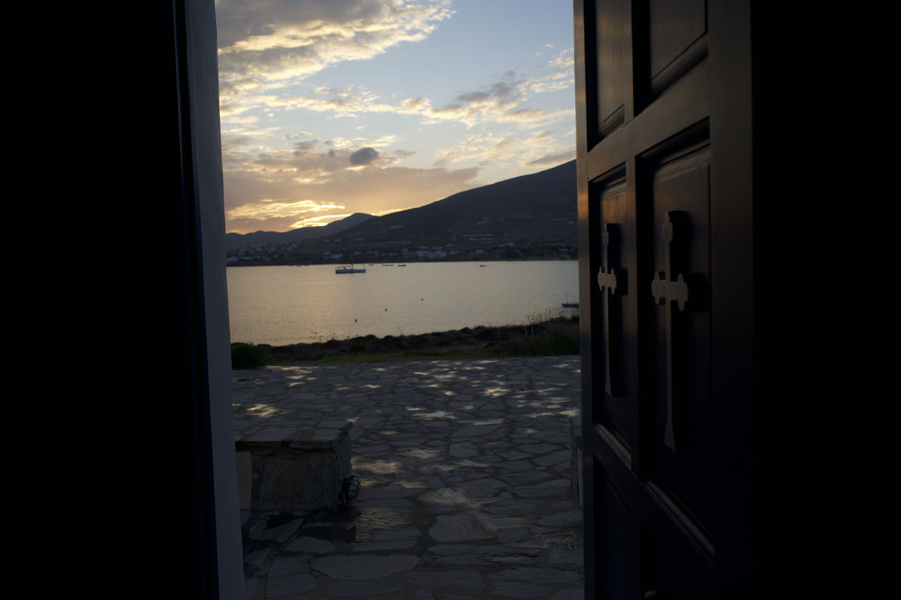 sky, cloud, water, window, nature, scenics - nature, door, mountain, architecture, no people, entrance, sunset, light, beauty in nature, darkness, sea, reflection, tranquility, mountain range, building, outdoors, building exterior, built structure, sunlight, tranquil scene, house, open, glass