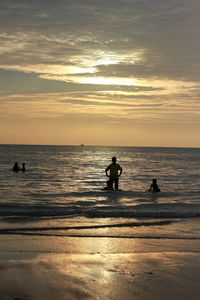 Silhouette people swimming in sea against sky during sunset