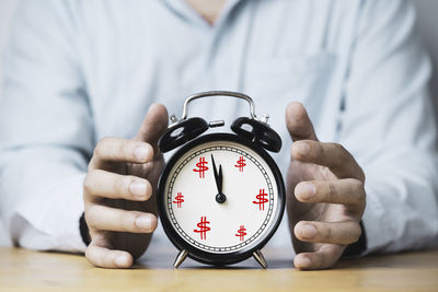 Close-up of hand holding clock on table