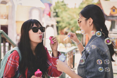 Female friends blowing bubbles in city