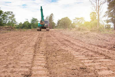 Tractor on dirt road amidst field against sky