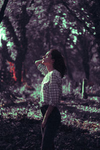 Side view of woman standing by tree in forest