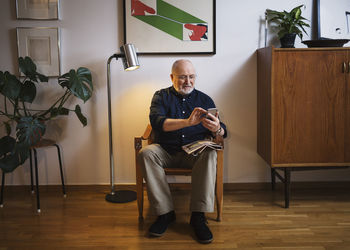 Senior man using mobile phone on chair at home