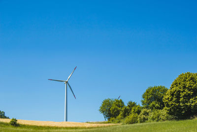 Windmill on field against clear blue sky