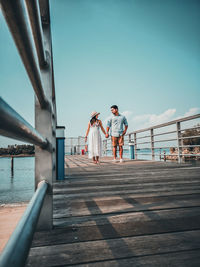 Rear view of couple walking on railing against sky