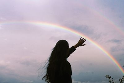 Low angle view of woman standing against rainbow in sky