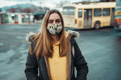 Portrait of young woman wearing mask standing in city during winter
