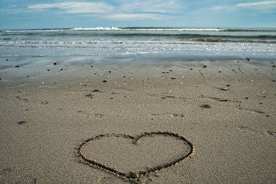 Heart shape on sand at beach against sky