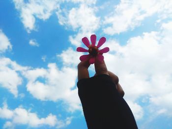 Copped hand holding flower against cloudy sky