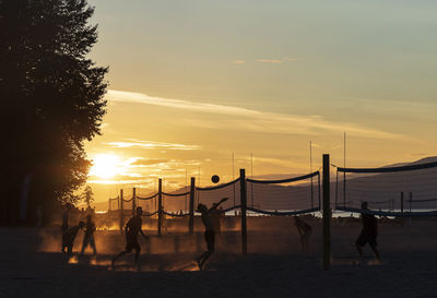 Silhouette people playing beach volleyball against sky during sunset