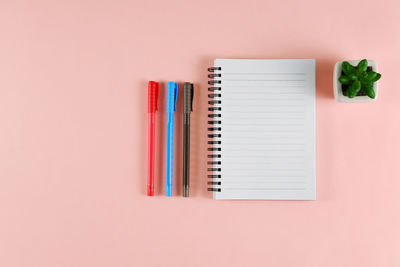 Directly above shot of diary and pens on pink background