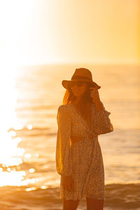 Side view of woman standing at beach against sky during sunset