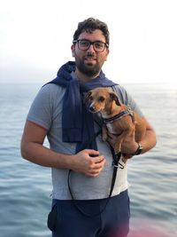 Portrait of man holding dog against sea