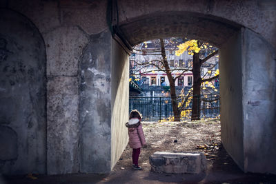 Girl standing below archway against trees