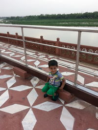 Boy sitting on railing by water