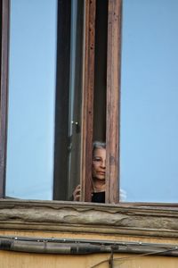 Portrait of woman standing by window against blue sky