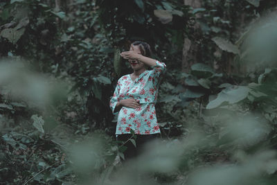 Smiling woman hiding eyes while standing in forest