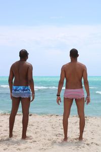Rear view of shirtless men standing at beach