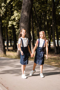 Two elementary pupils smile and hold hands and go to school on a warm day. vertical view