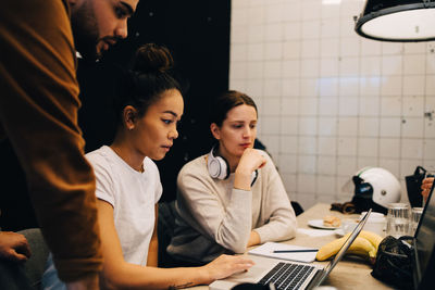 Confident young multi-ethnic colleagues discussing over laptop at office