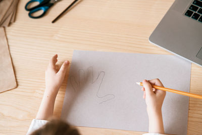 Child trace around a hand on paper with pencil using video lesson for drawing. distance education