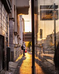 Rear view of woman walking on footpath amidst buildings in city