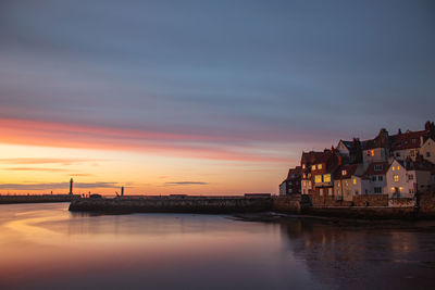 Scenic view of sea by buildings against sky at sunset