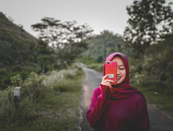 Portrait of woman holding red while standing against trees