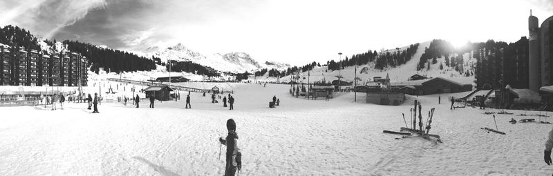 Panoramic shot of people skiing on snowy field against sky on sunny day