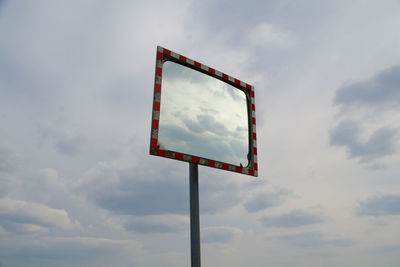 Low angle view of road mirror against cloudy sky