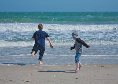 Full length of playful boys at beach against sky