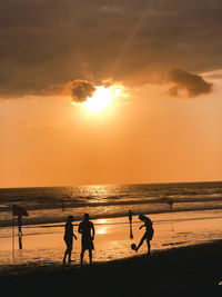 Silhouette people on beach against sky during sunset