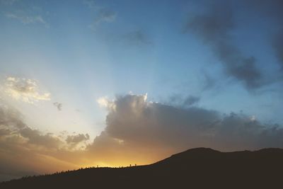 Sunlight streaming on silhouette mountain against sky during sunset