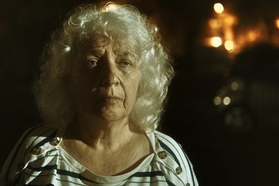 Portrait of an elderly grey-haired curly woman with long hair on the street of a night city.