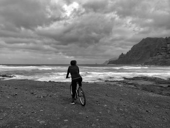 Rear view of man riding bicycle on beach