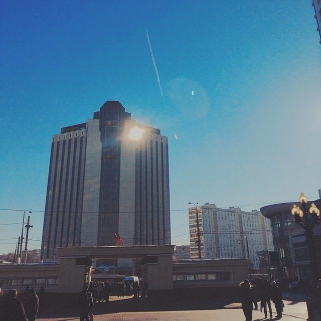 building exterior, architecture, built structure, city, clear sky, skyscraper, city life, transportation, low angle view, office building, tall - high, modern, sky, mode of transport, blue, land vehicle, car, building, street