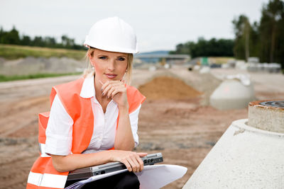 Portrait of architect in reflective clothing sitting on dirt road against sky