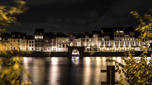 Illuminated buildings by river against sky at night