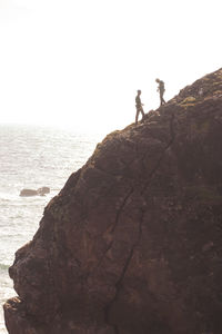 People on rock by sea against clear sky