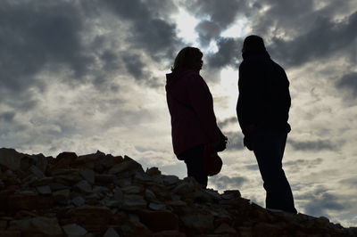 Low angle view of silhouette rock formation against cloudy sky