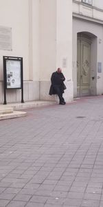 Rear view of man walking on sidewalk by building